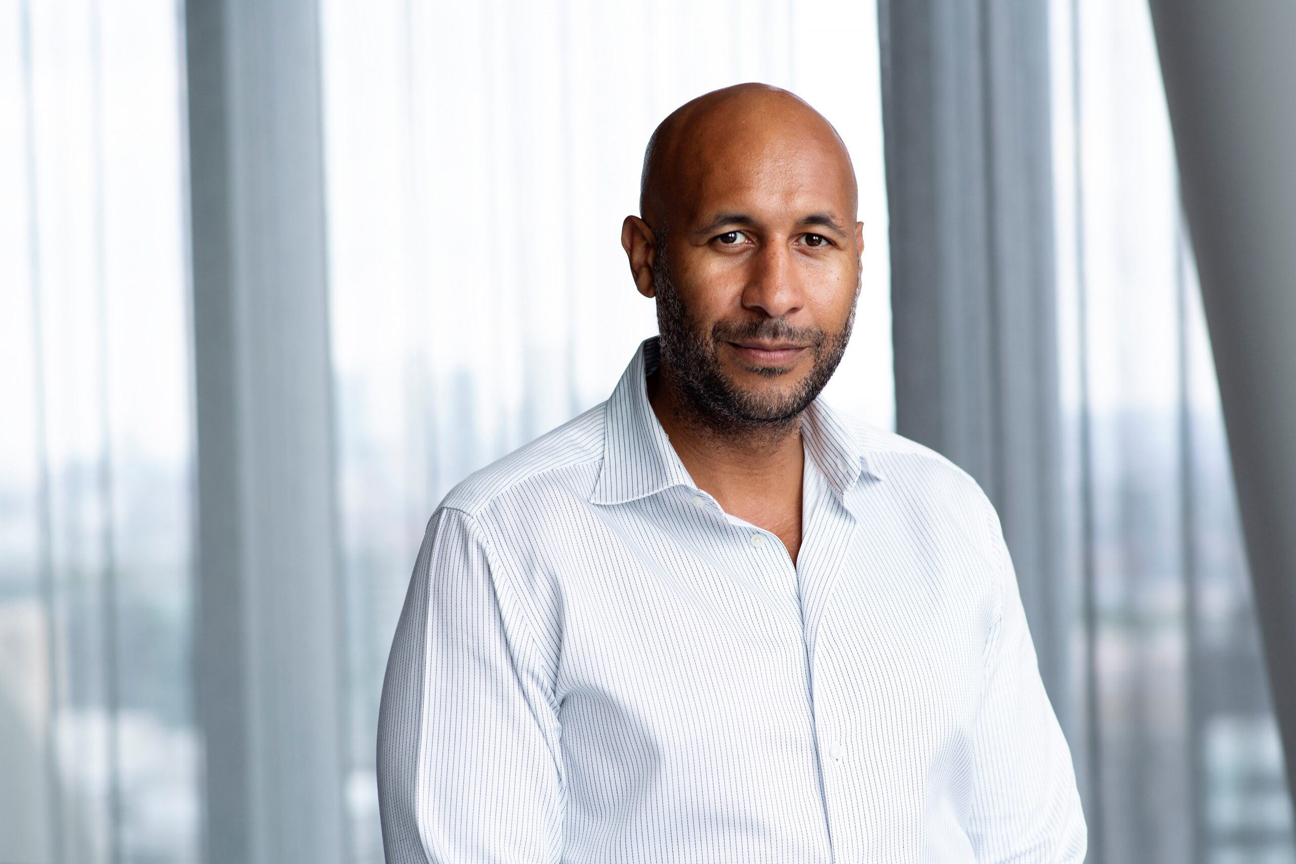 A profile shot of Thomas sitting in front of a window, dressed in a white shirt facing the camera.